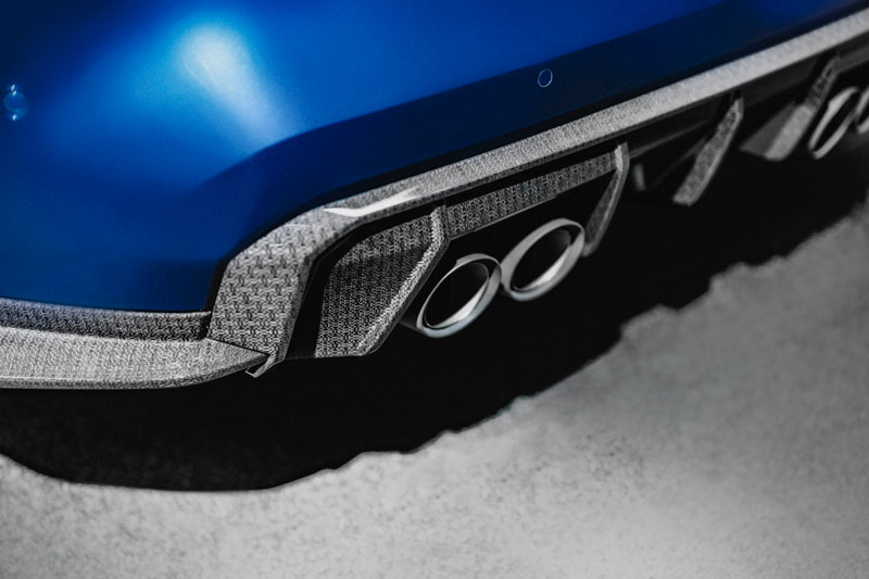 A weave patterned, green body part surrounding an exhaust pipe of a blue car