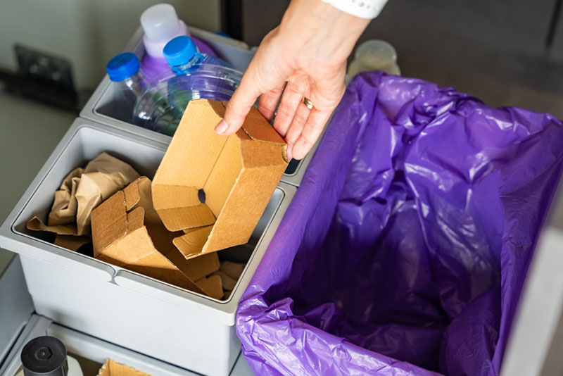 Hand of woman throwing trash into household bins for waste sorting in the kitchen for recycle. Plastic, paper, bio and mixed waste