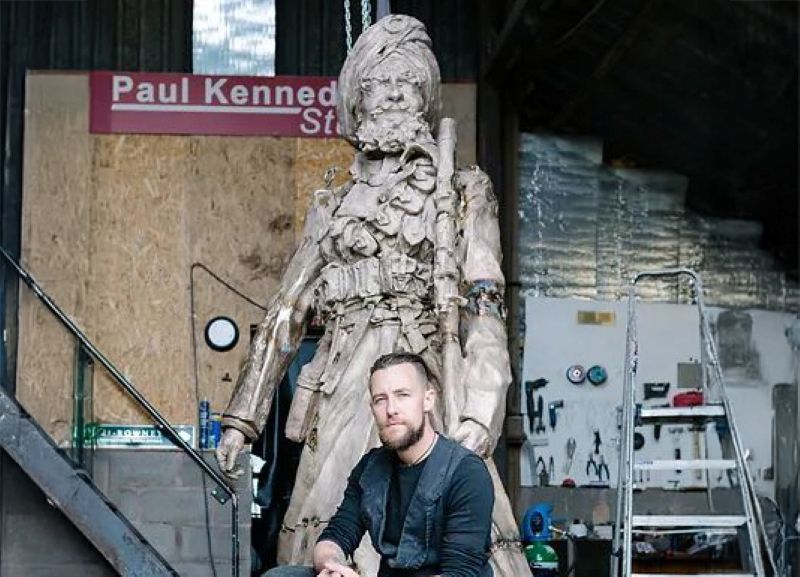 Luke Perry seated below a Sikh Soldier sculpture in metal pictured.