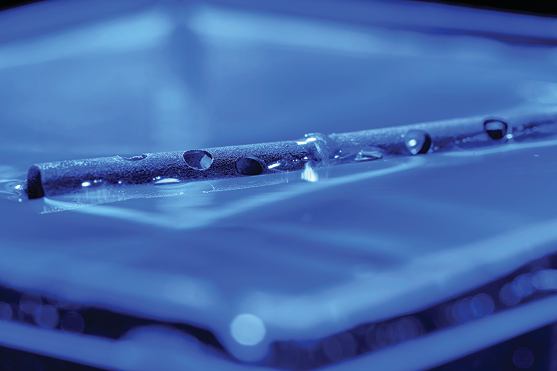 Blue-tinged image of a chemically etched aluminium tube floating in a tub of water