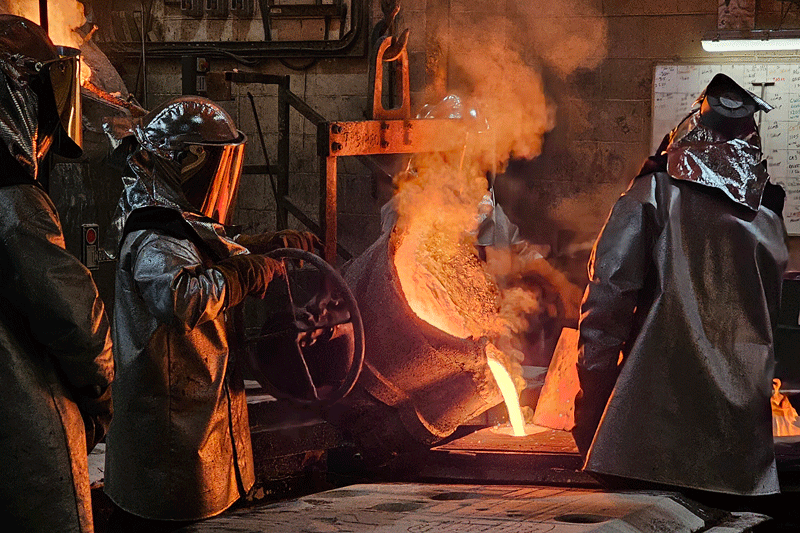 People in protective clothing pouring out melting liquid into a cast