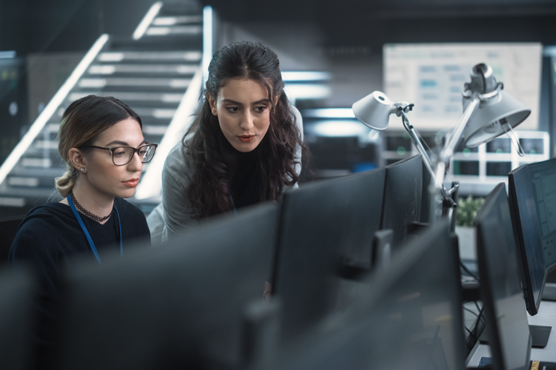 Stock image of two women working in an office, surrounded by computers