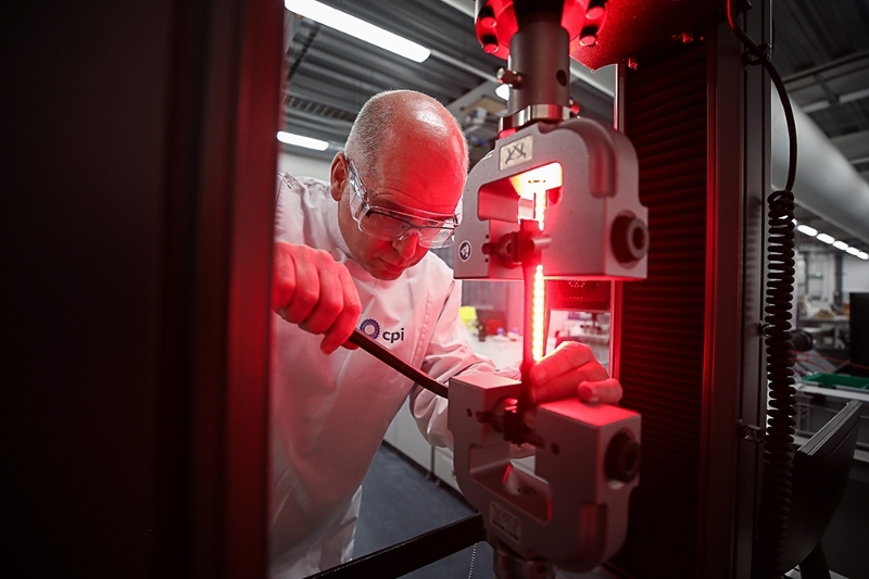 Employee working at CPI's National Formulations Centre, he has a white lab coat and goggles and appears to be using a screwdriver to adjust machinery
