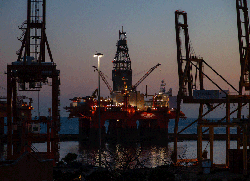 Drilling rig flanked by cranes in the twilight