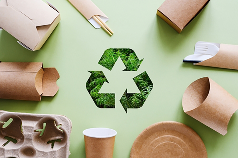 Various packaging items surrounding a large version of the recycling sign - which is three arrows that go around the outside of negative space that makes a triangle