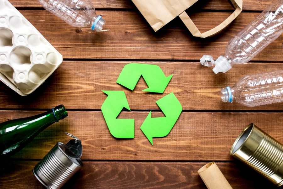 Recycling symbol with packaging waste surrounding it on wooden background top view