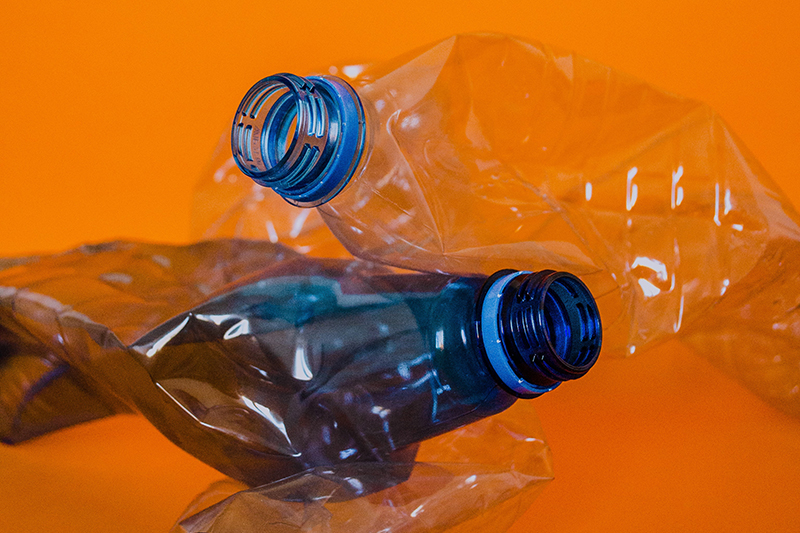 crushed single use pastic bottles in a pile on an orange background