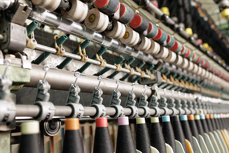 Stock image of an industrial loom with yarn spools and thread feeding system