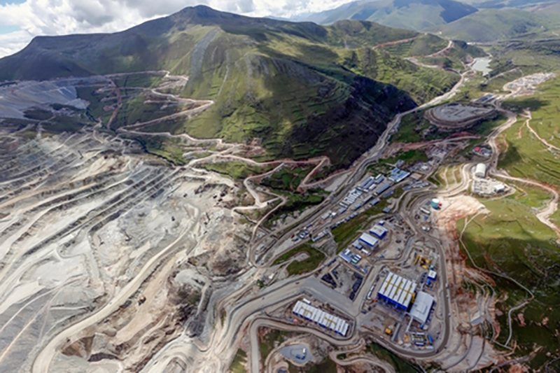 A birds-eye view of a huge mining operation carved into and around the side of a mountain with vegetation on and lots of zig-zagging dirt roads 