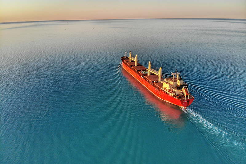 a long distant shop of a large ship heading across open water with sun setting