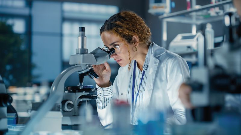 Woman looking through a microscope in a lab coat