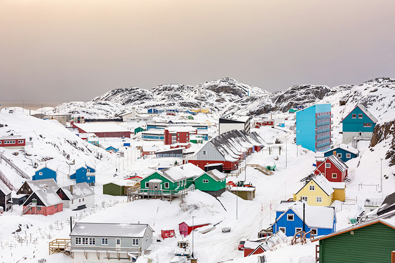 View over the town of Maniitsoq, Greenland. Colourful houses and flats against a hilly snow covered landscape