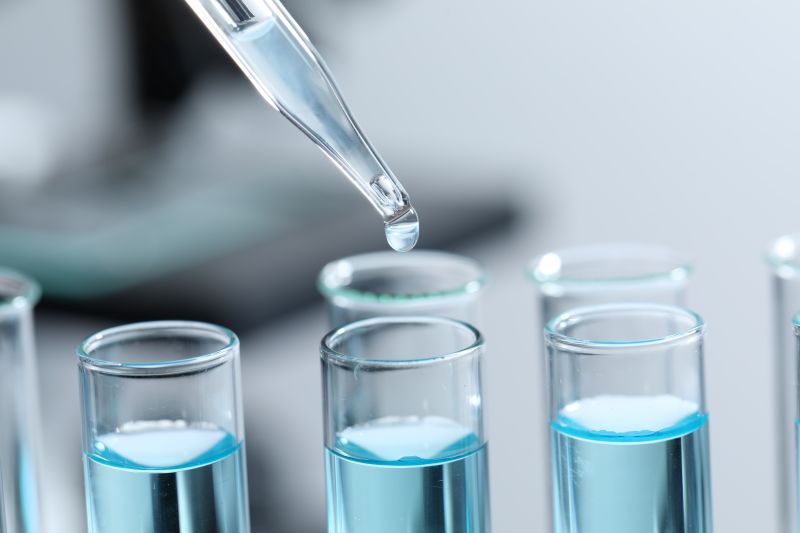 Dripping liquid from pipette into test tube on blurred background, closeup pictured