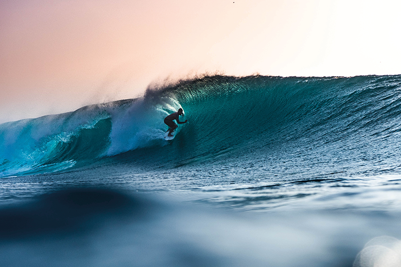 Stock image of a surfer in a wave against a pink sunset