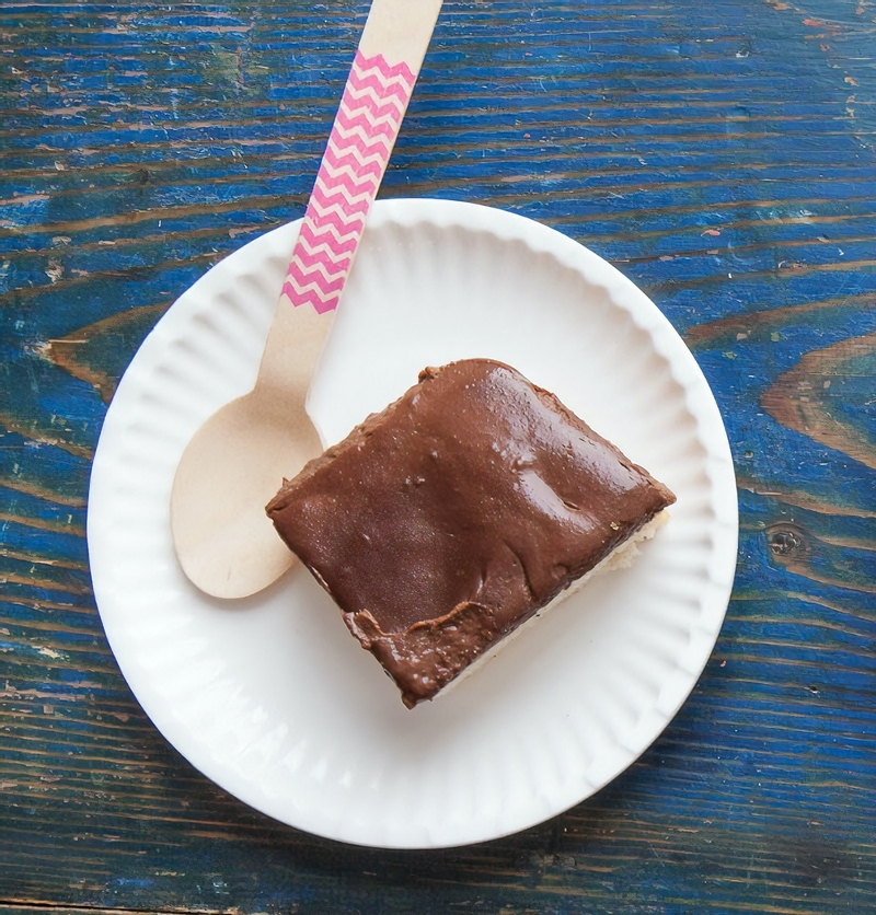 Cake with chocolate icing on a paper plate with a wooden spoon