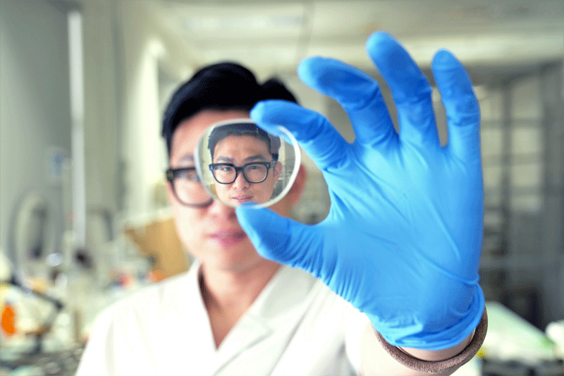 PhD student Sun Ye looks through a plastic lens  with the new self-cleaning, anti-fogging coating 