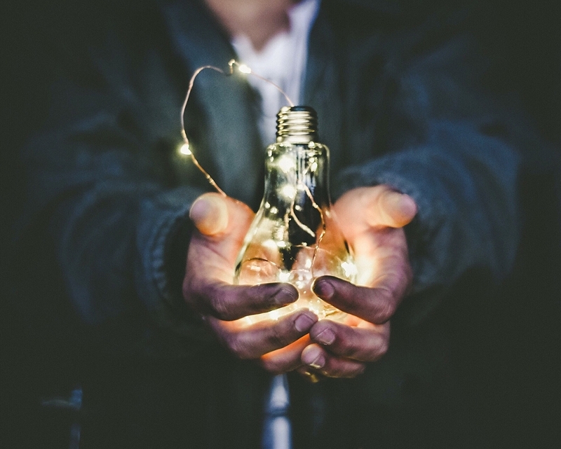 person in a jumper and shirt holds a glowing bulb in their hands, shot only shows torso