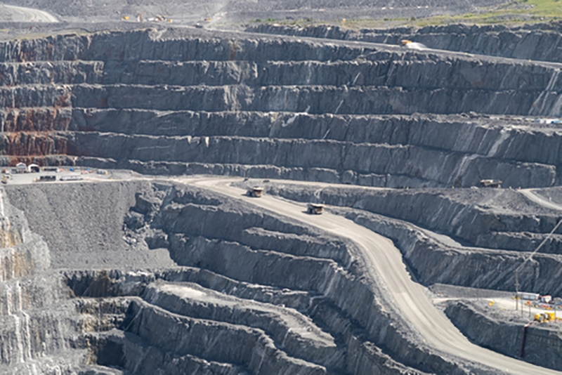 Mining trucks in the distance driving along narrow mining roads that concertina down the side of a huge open pit quarry in Canada