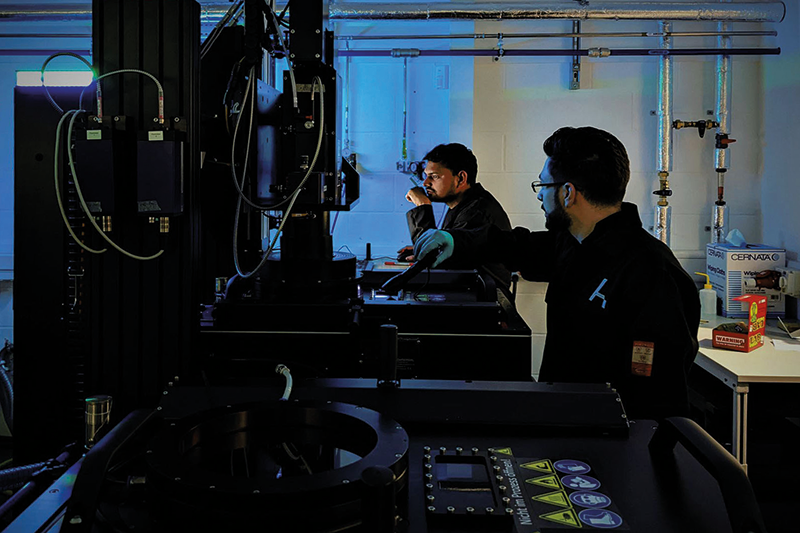 Two Alloyed team members operating an additive manufacturing machine in a dark room