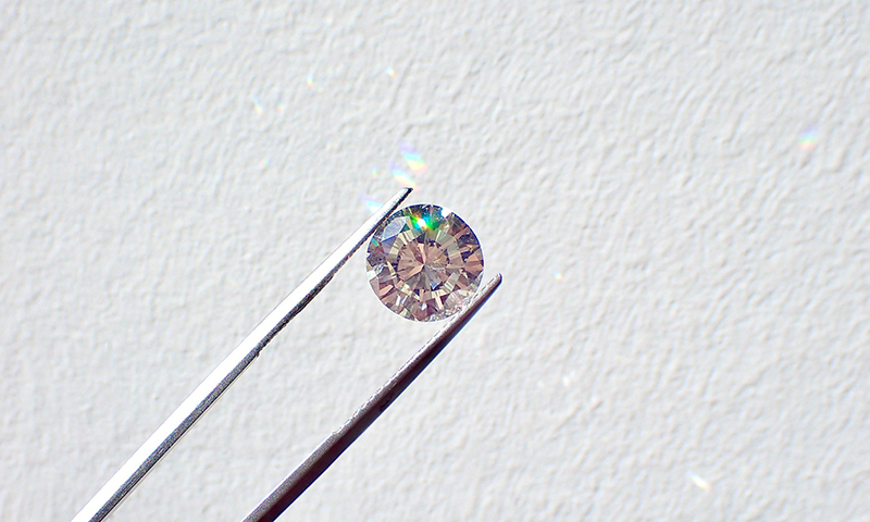 Cut diamond held between tweezers against a white wall