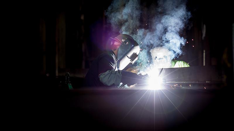 Darkness with a welder in full kit illuminated by sparks
