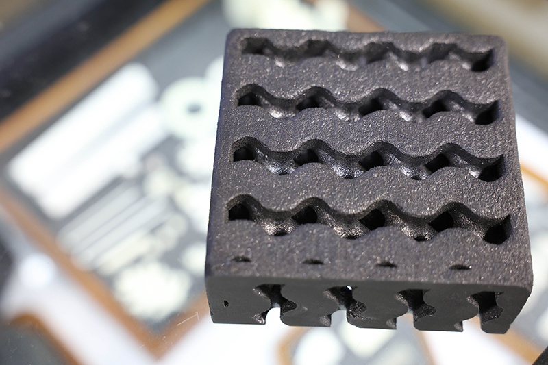 A dark grey block of silicon carbide, 3D printed with squiggly and porous patterns