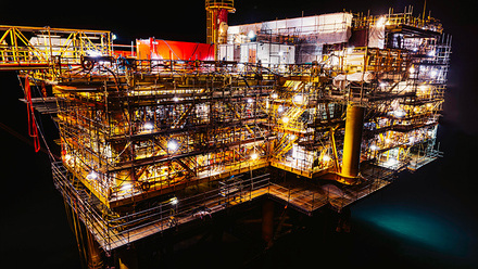 An oil rig at night. Each level is illuminated by bright lights, highlighting the scaffolding-like structure