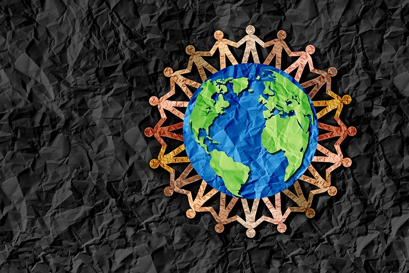 Stock image of a paper cutout of the world surrounded by people holding hands