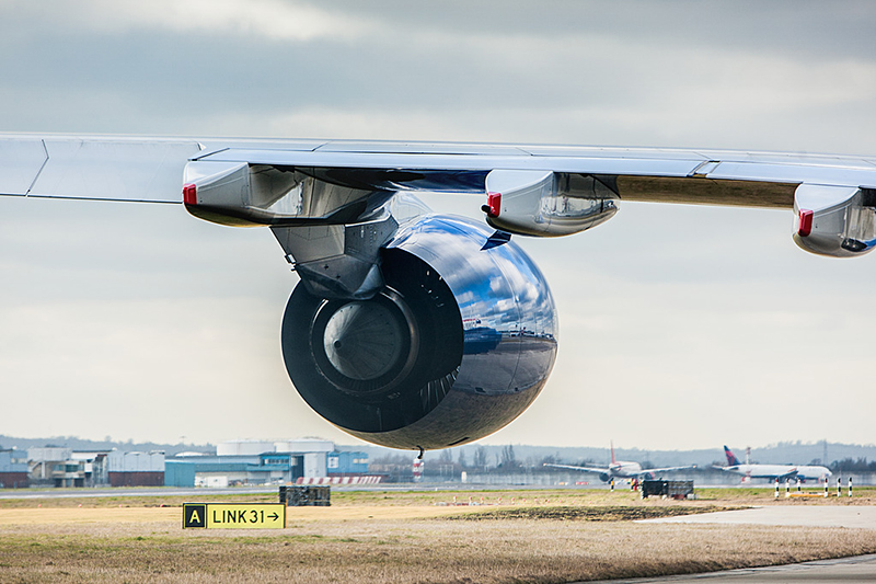 The jet engine of a plane and its wing with planes in the distance at an airport