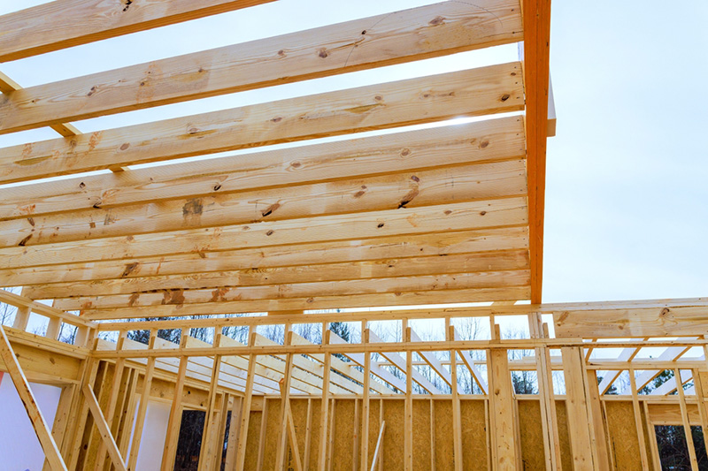 Workers are assembling wooden beams framework at construction site surrounded by roof timber