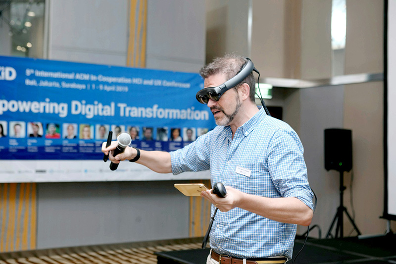 A white male with a beard in a blue shirt holding a VR controller and wearing a VR headset