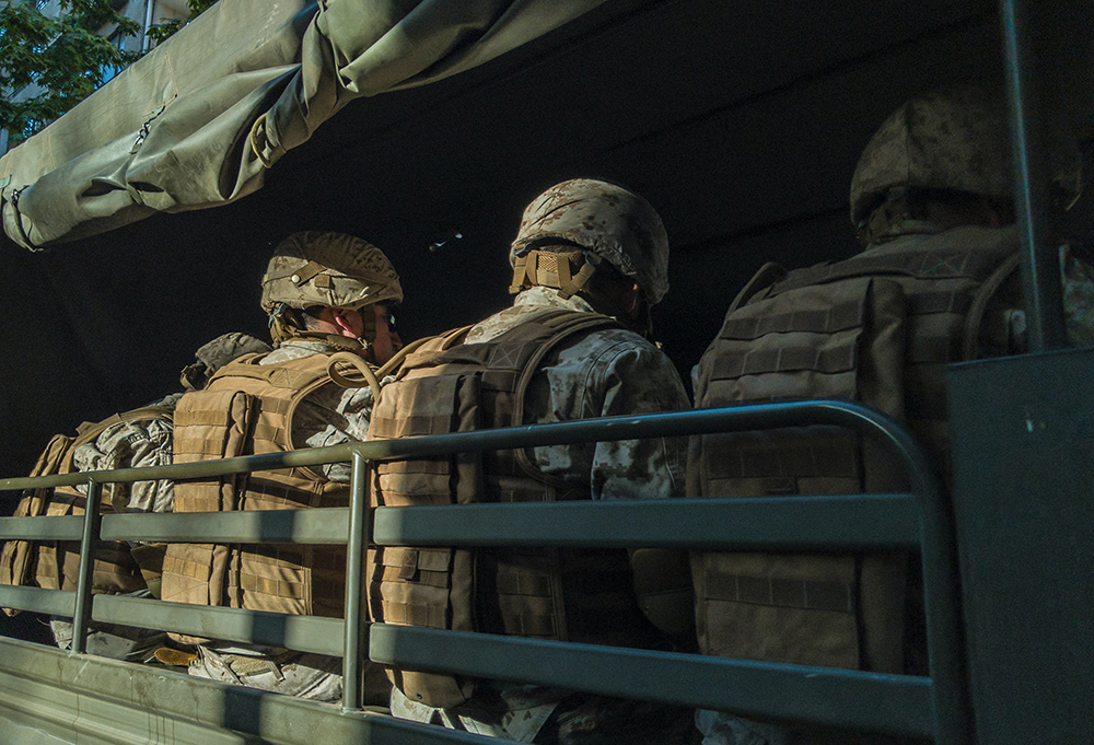 Soldiers in a vehicle seen from the rear, four uniformed and helmeted people are seen seated