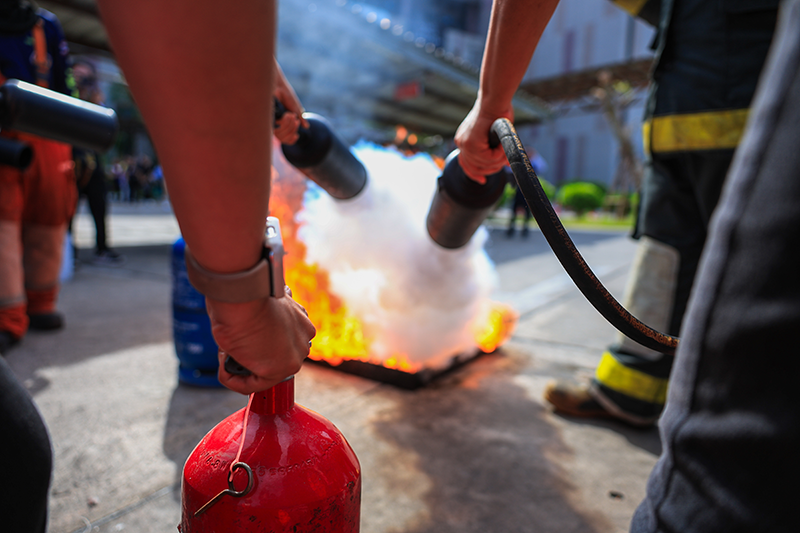 Stock image of employees undertaking fire safety training, spraying a small controlled fire with extinguishers