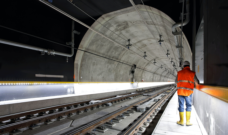 Rial tunnel with tracks to the left and a worker in high-vis clothing with hard hat on a narrow platform to the right