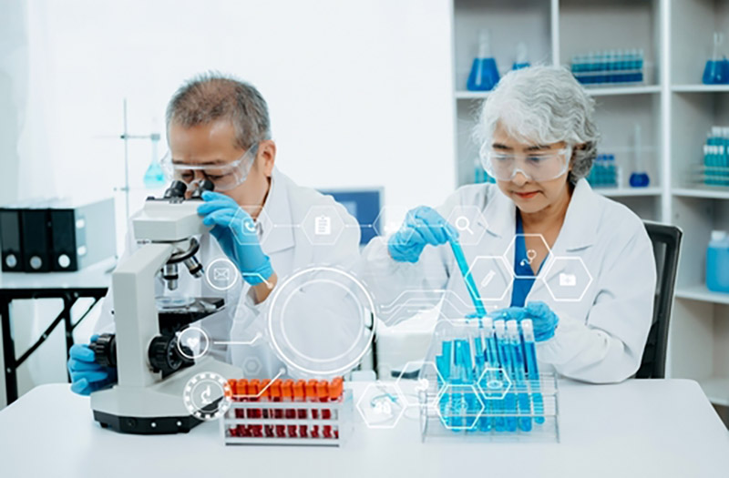 Two older scientists  sitting at a lab table with a microscope and pipettes
