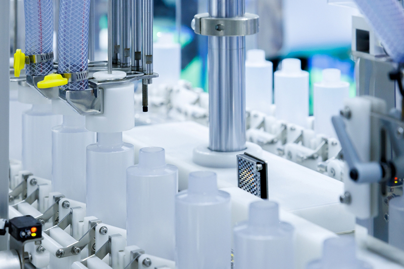 robot arm moving plastic bottles to the conveyor belt of an auto capping and labeling machine at cosmetic and skin care factory