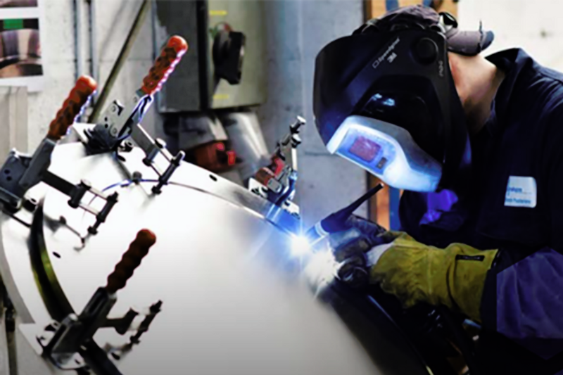 A welder in protective blacksmith mask and gloves welds the hatch of a metal container