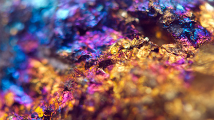 Macrophotograph of mineral containing gold, copper and iron ores in the form of gold, blue and purple crystals