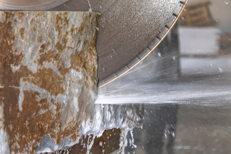 A close up of part of a circular machine saw cutting through stone with water spraying off it