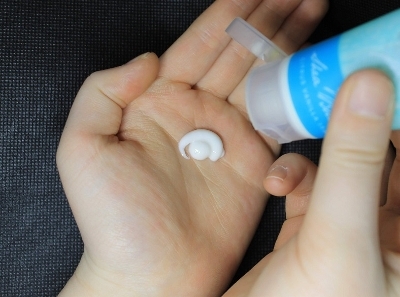 Hand cream in a blue tube being squeezed onto a left hand by the right