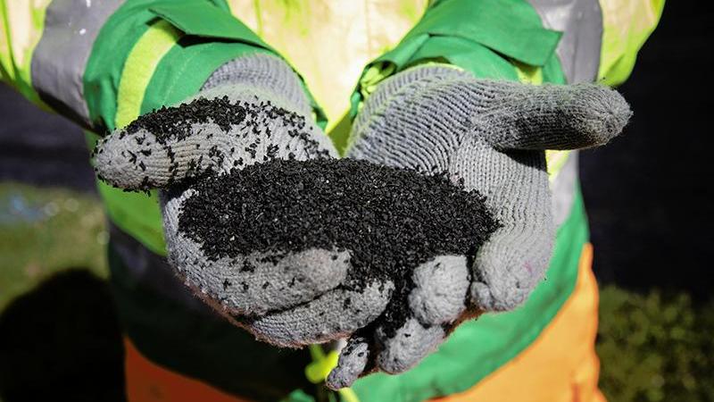 Close up of gloved hands holding a black powder. The person is wearing safety clothing.