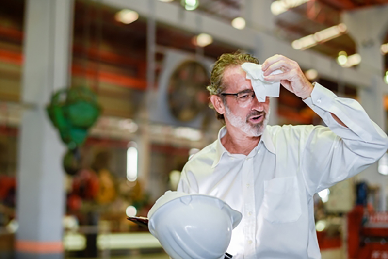 Man in shirt taking off hard hat and wiping brow as too hot