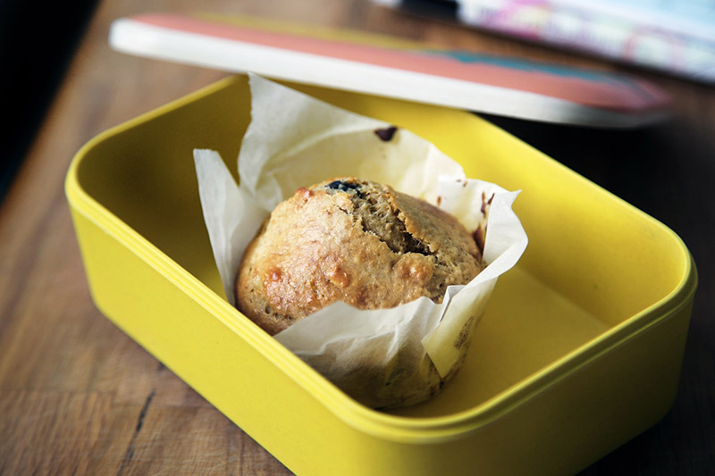 mustard yellow sandwich box containing a sweet muffin in a folded paper case