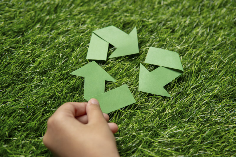 A child’s hand holding a green paper arrow forming a triangular loop on a grassy background.