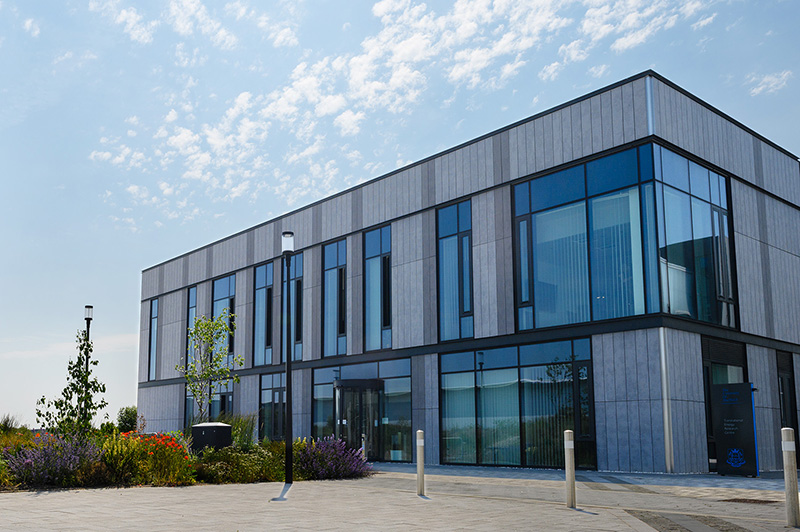 Squat grey building with plants in front and pathways