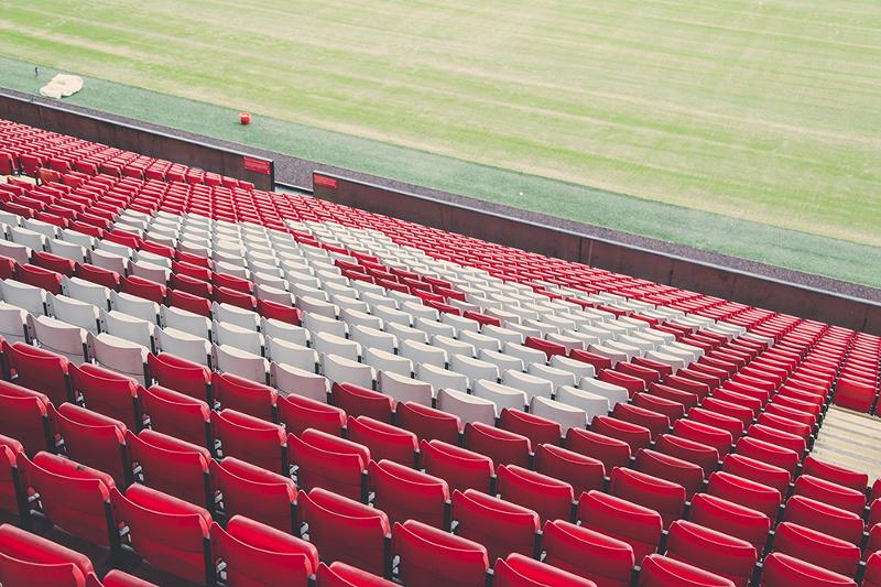 red and white seats sloping down to the pitch at Anfield stadium