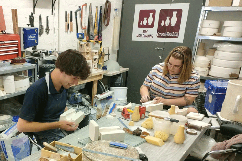 Two people on a table working on a white mould