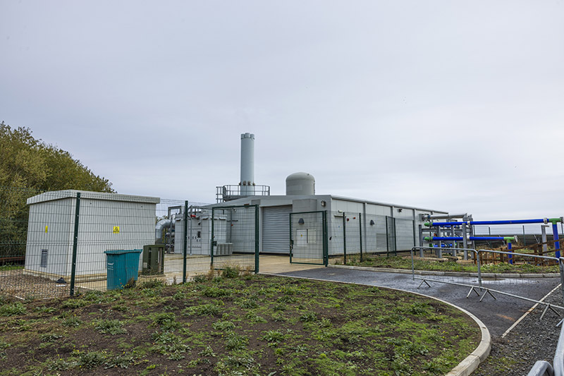  A picture of the energy centre, which is a one-story small building with a chimney and another industrial tank behind fencing
