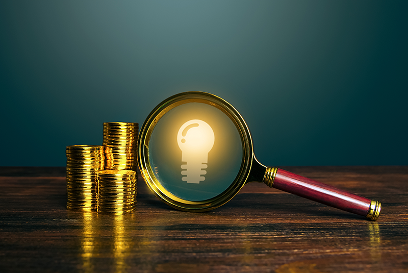Stock image of a magnifying glass next to stacks of coins