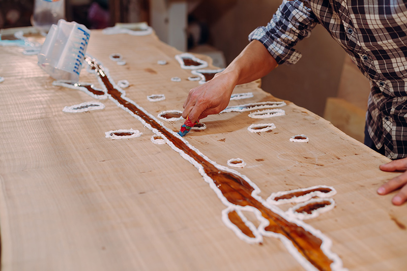 Carpenter cleaning epoxy resin drops from a wooden table in a workshop